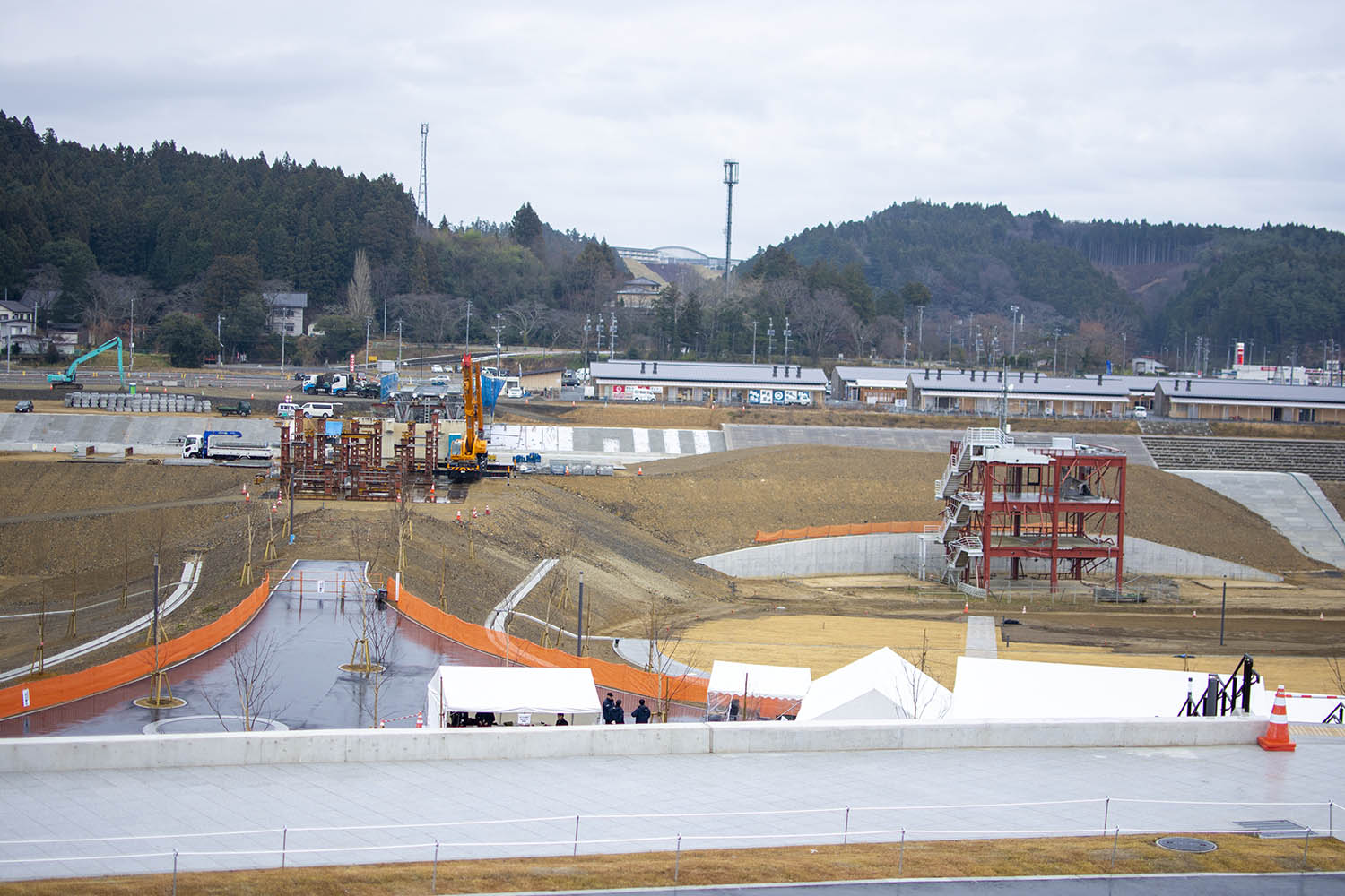 クレーン車やトラックが並び鉄骨の構造物が新たに建設され、赤茶色の骨組みだけが残った4階建ての建物があり、東日本大震災の被災地で整備が進められている様子の写真