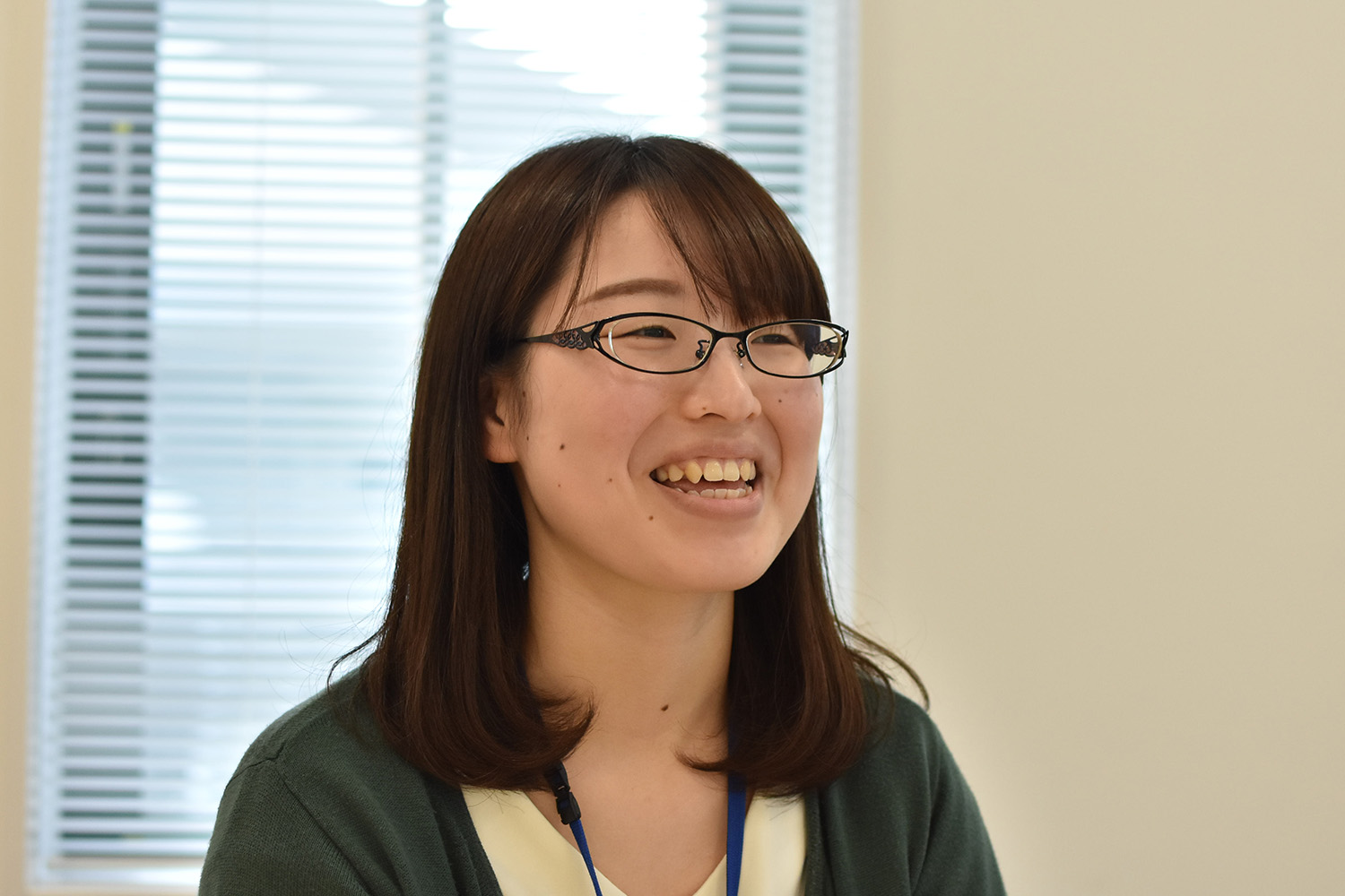 眼鏡をかけた女性が室内で笑顔を見せながら話している様子を写した写真