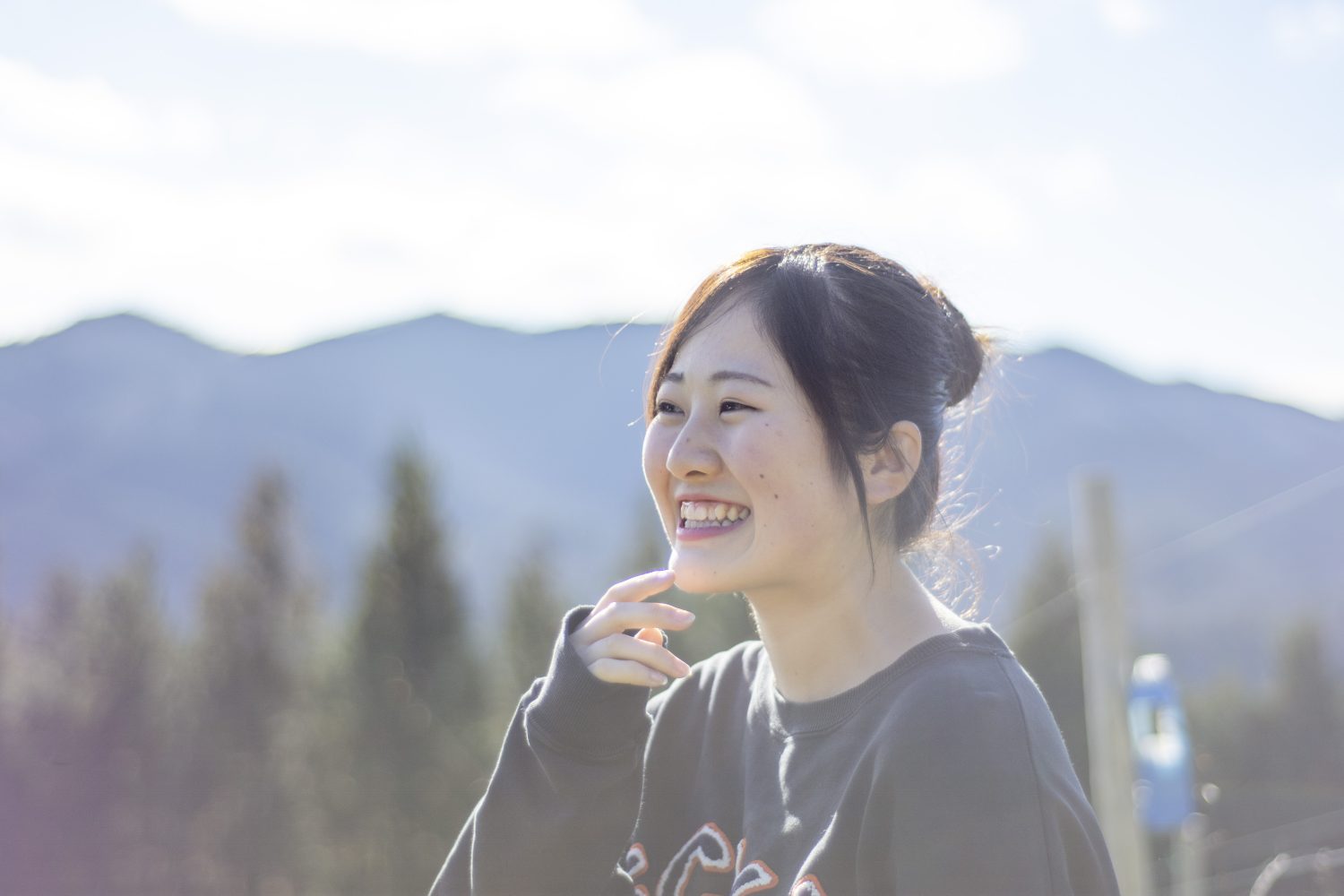 背景には青空と山々が広がり、笑顔の大沼ほのかさんを横から撮影した写真