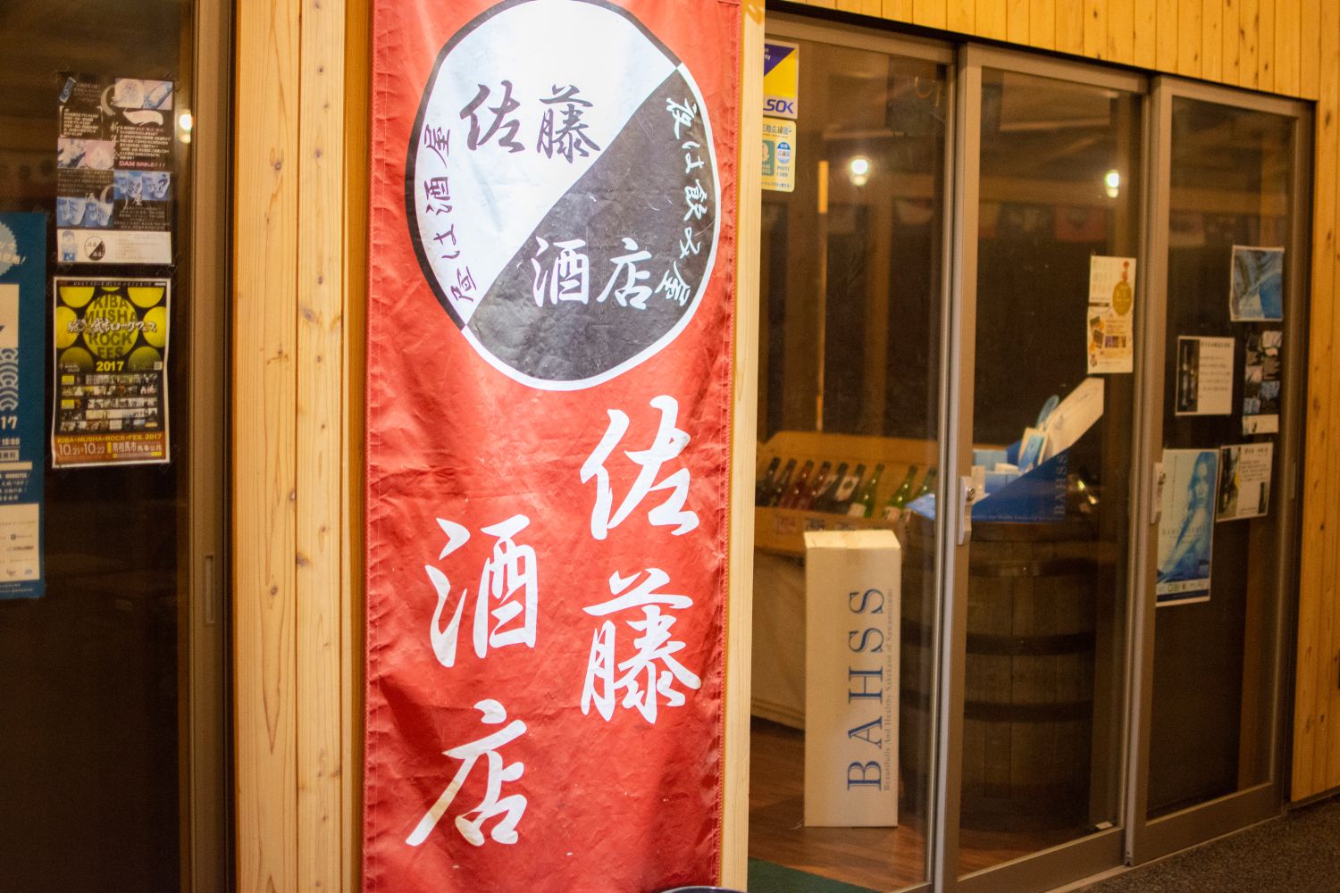 木製の外壁の建物の前に、「佐藤酒店」と白い文字で書かれている赤い縦長ののぼりが飾られている写真