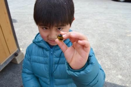 水色のダウンジャケットを着た男の子が、右手で完成したガラス玉を持ちカメラに向かって見せている様子の写真