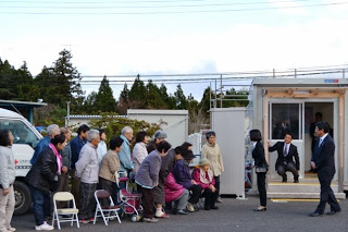 プレハブの建物の前で三笠宮家彬子女王殿下と佐藤町長が、集まっていた多くの地域住民に向かって挨拶をしている様子の写真