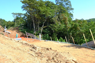 斜面の上で作業員が整地作業を進めており、まわりには土留め用の柵や囲いがあり、道路工事の準備が進められている様子を写した法面整備中の写真