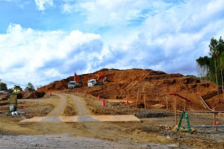 茶色い土の山に向かう坂道の左右でショベルカーやトラックが作業をしている造成現場の写真