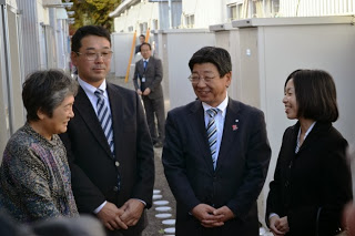 仮設住宅の通路で三笠宮家彬子女王殿下と佐藤町長が地域の高齢女性と話し交流している様子の写真