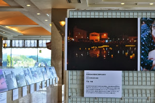 会場内の壁面に夜の灯篭流しの写真が展示されている様子の写真