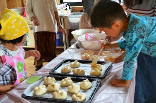 男の子がはけでパン生地に卵液を塗っている様子を、女の子が近くで見ているパン作り教室の写真