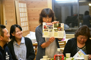 お店が紹介されている冊子を皆に見せ話をしている民子さんの写真