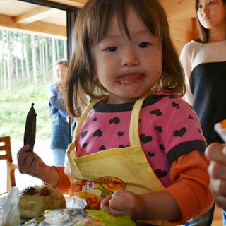 ピンクのハート柄の服を着た幼い女の子が、手にチョコペンを持ち、口の周りにチョコレートをつけて写っている写真