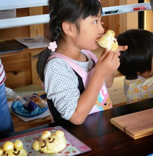 三つ編みの髪の女の子が、出来上がったパンを両手で持ち食べている様子の写真