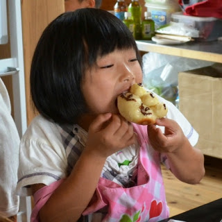エプロンをつけた女の子が出来上がったパンにかぶりついている様子の写真