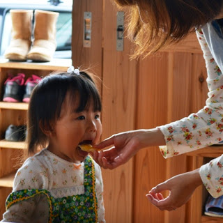 小さな女の子が口を大きく開けて、パンを口に入れてもらっている写真