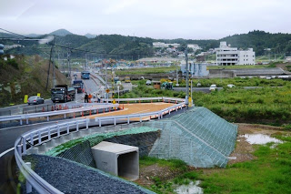 緑の田園が広がり、建物が点在する中を通る道路から、分岐した道路がカーブを描いて続いている様子の写真