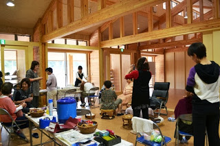 広い木造の室内で、参加者が談笑したり、足や肩のマッサージを受けながら交流している様子を写した写真