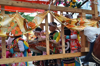 木製の山車の中で、色鮮やかな祭りの衣装を身にまとった子どもたちが太鼓を演奏している様子を写した写真