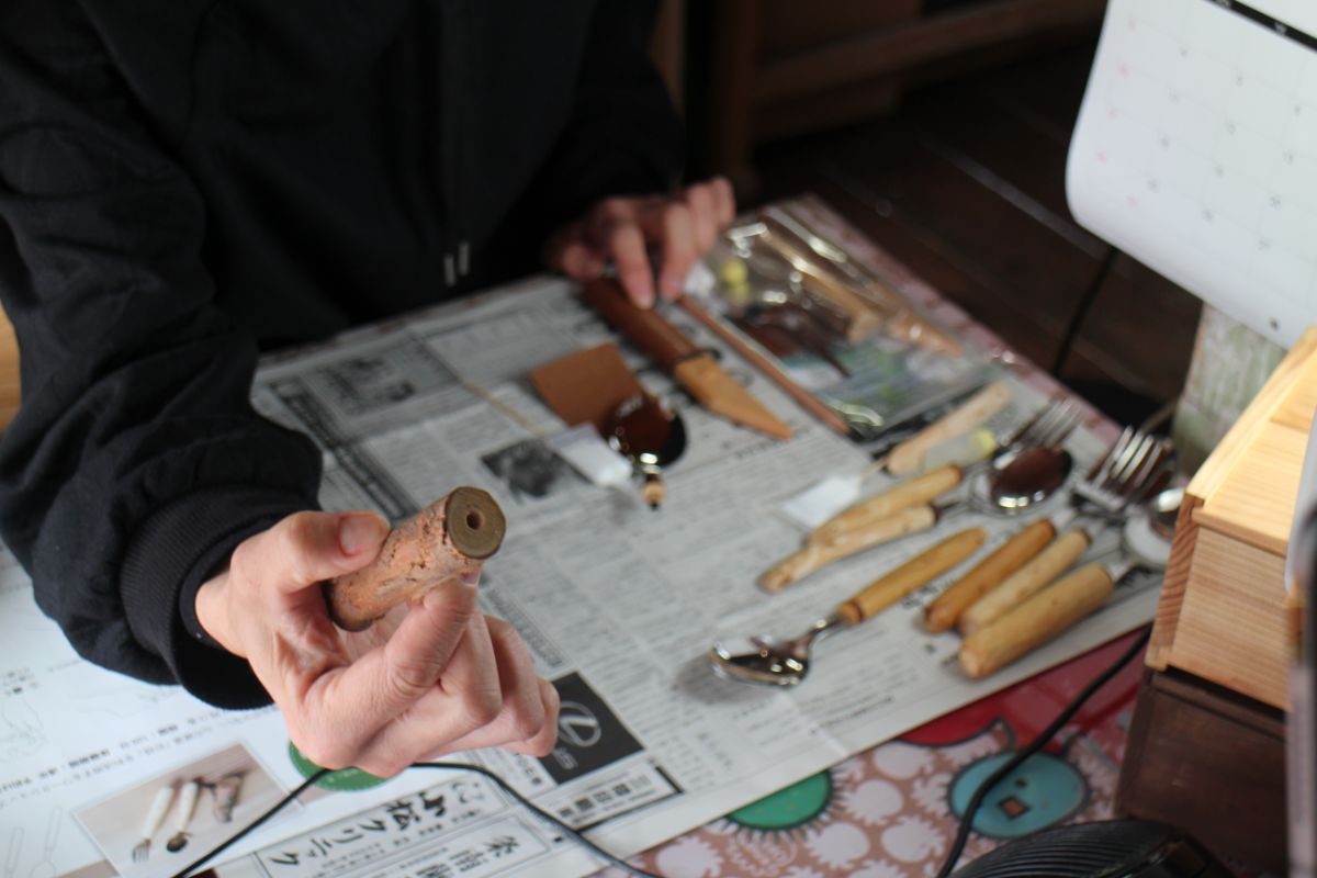 作業テーブルにナイフやフォークの持ち手の部分が並べられ、黒い服の人物が木製の持ち手を手に持っている写真