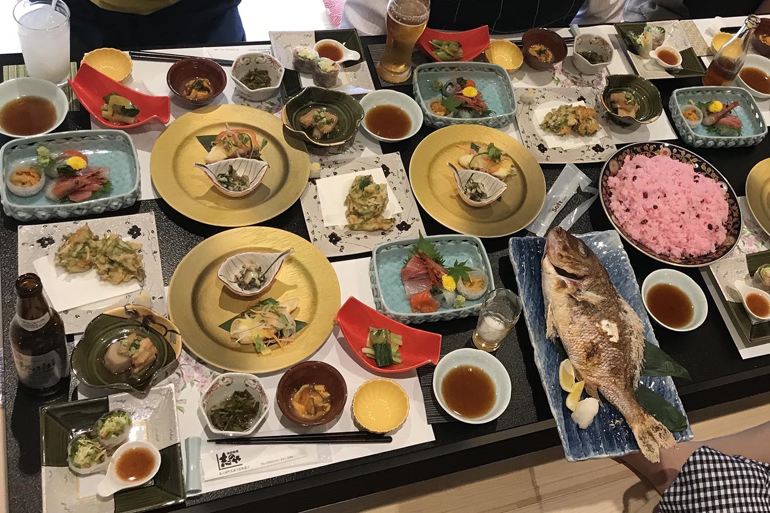 テーブルの上に鯛の尾頭付き、赤飯、刺し身などの豪華な料理が並べられた写真