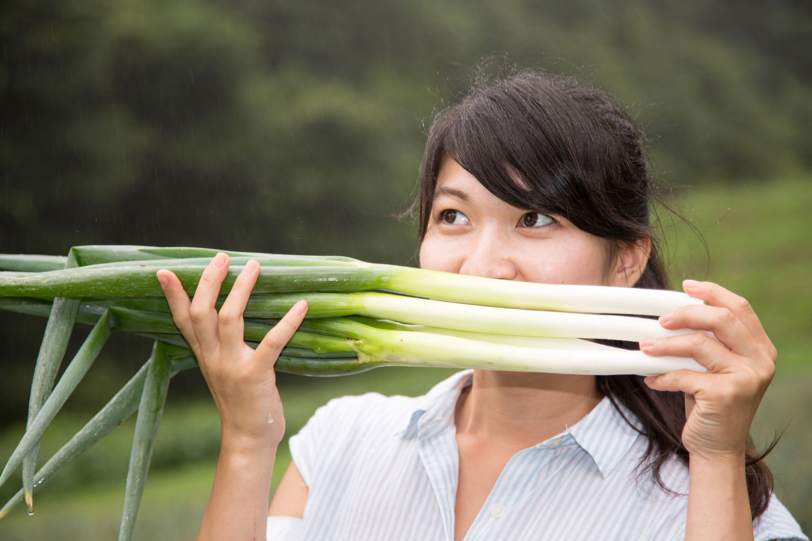 女性が両手に束ねた複数本の長ネギを顔に近づけて香りを嗅いでいる様子の写真