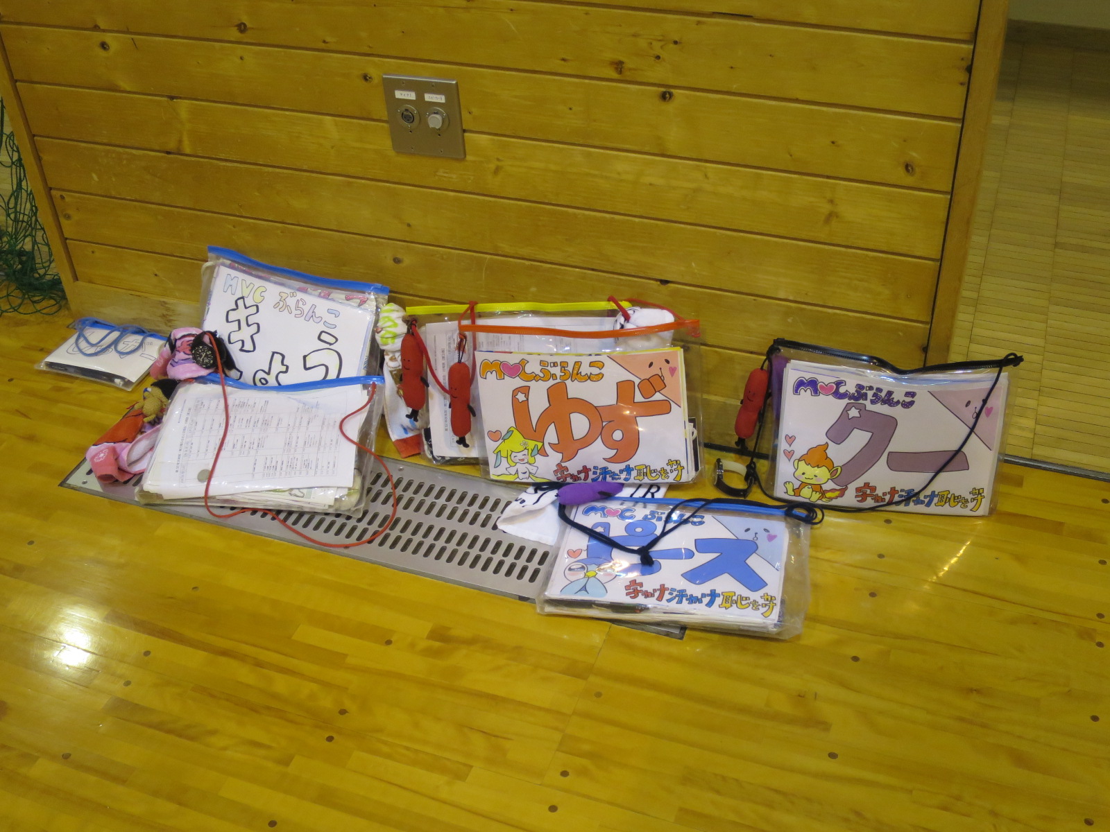 透明なビニールケースに名前やイラストが描かれた色紙や書類が床にまとめて置かれている写真