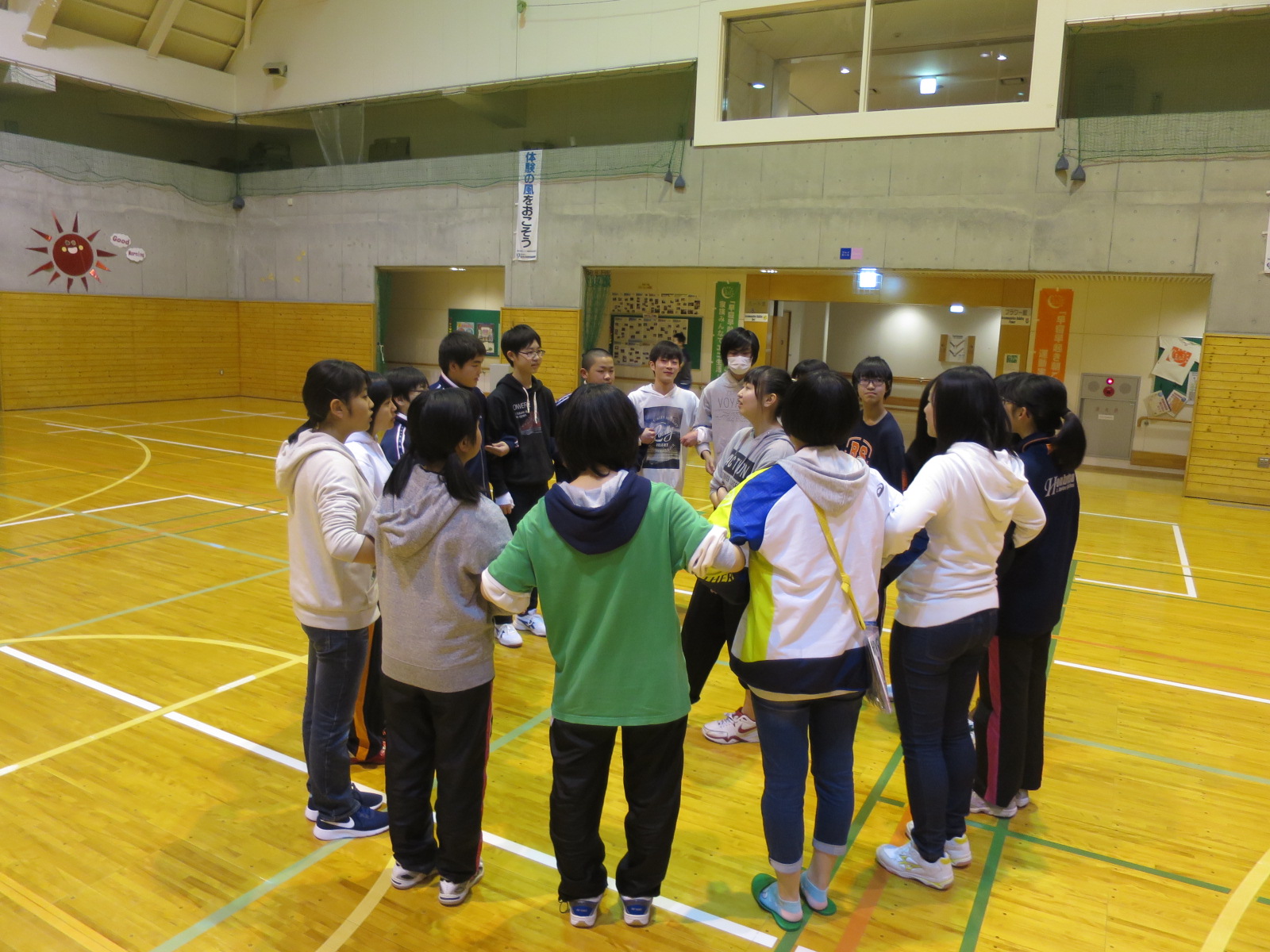 体育館集まったジュニアリーダーたちがお互いの腕を組んで大きな輪を作っている写真