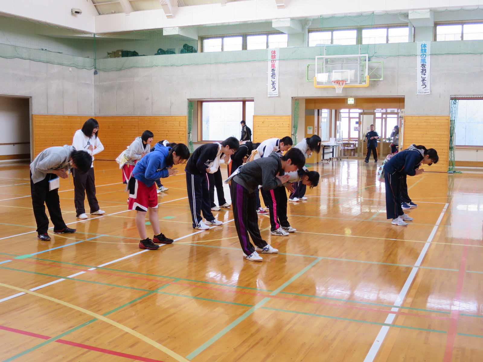 体育館に整列しているジュニアリーダーたちが、肩幅に両足を開き両手を胸の前で合わせ、前方に腰を曲げてストレッチをしている様子の写真
