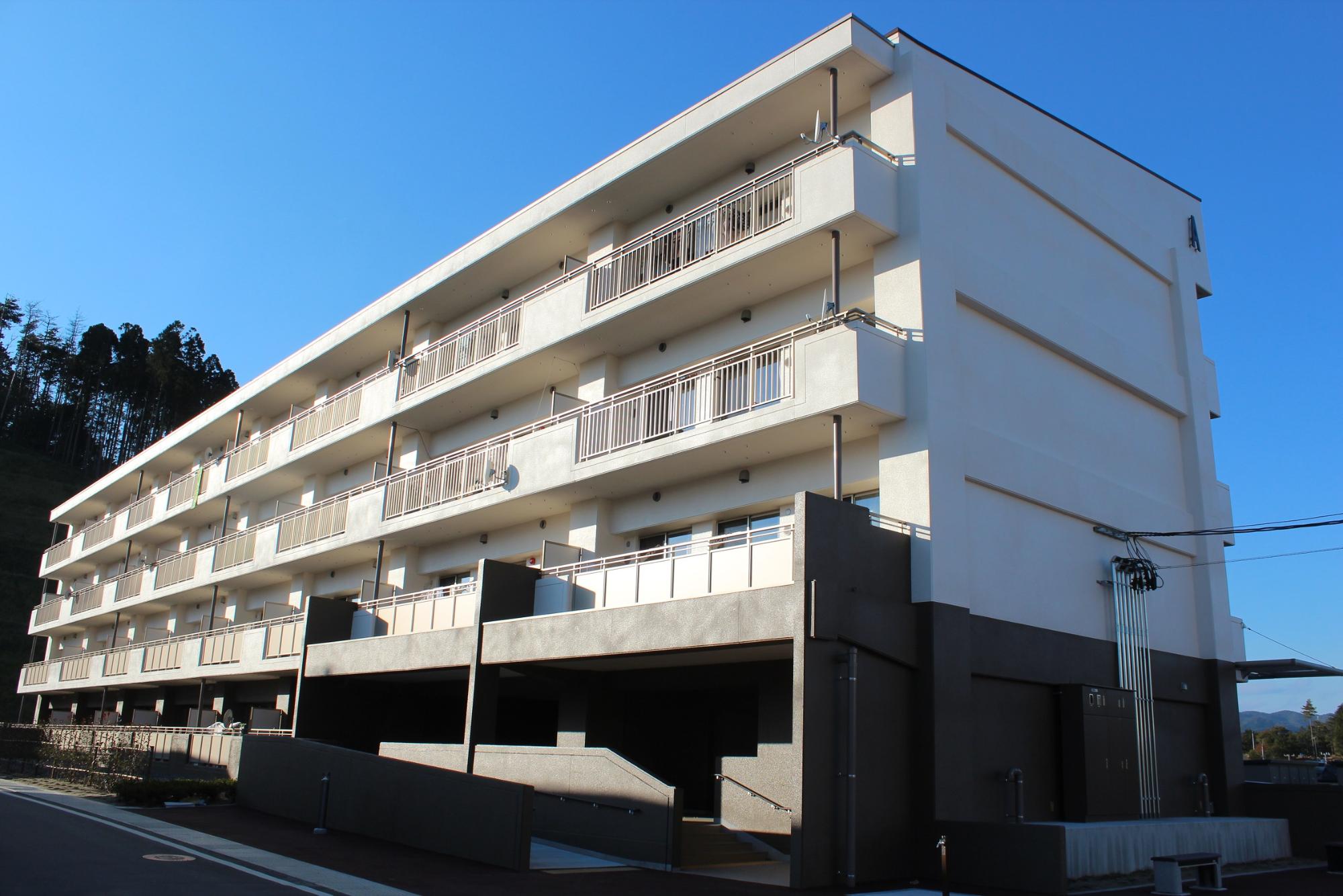 青空の下、斜めから見上げる角度で撮影された、白とグレーを基調とする4階建ての新しい集合住宅の写真