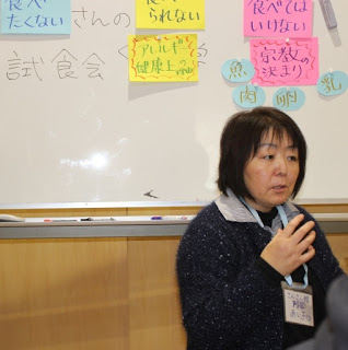 資料が貼られたホワイトボードの前に座っている阿部さんが話をしている写真