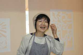 グレーのエプロンをつけた小泉さんが笑顔で話をしている写真