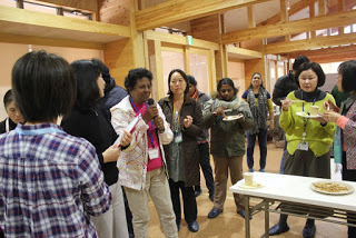 ジャイカの方々を交えた立食の試食会が行われる中、外国人の女性がマイクを持って話をしている写真