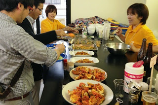 黄色のシャツを着た女性スタッフが見ているなか、カウンターの上に並んだホヤなどの料理を、参加者の男性がお皿にとりわけている様子の写真