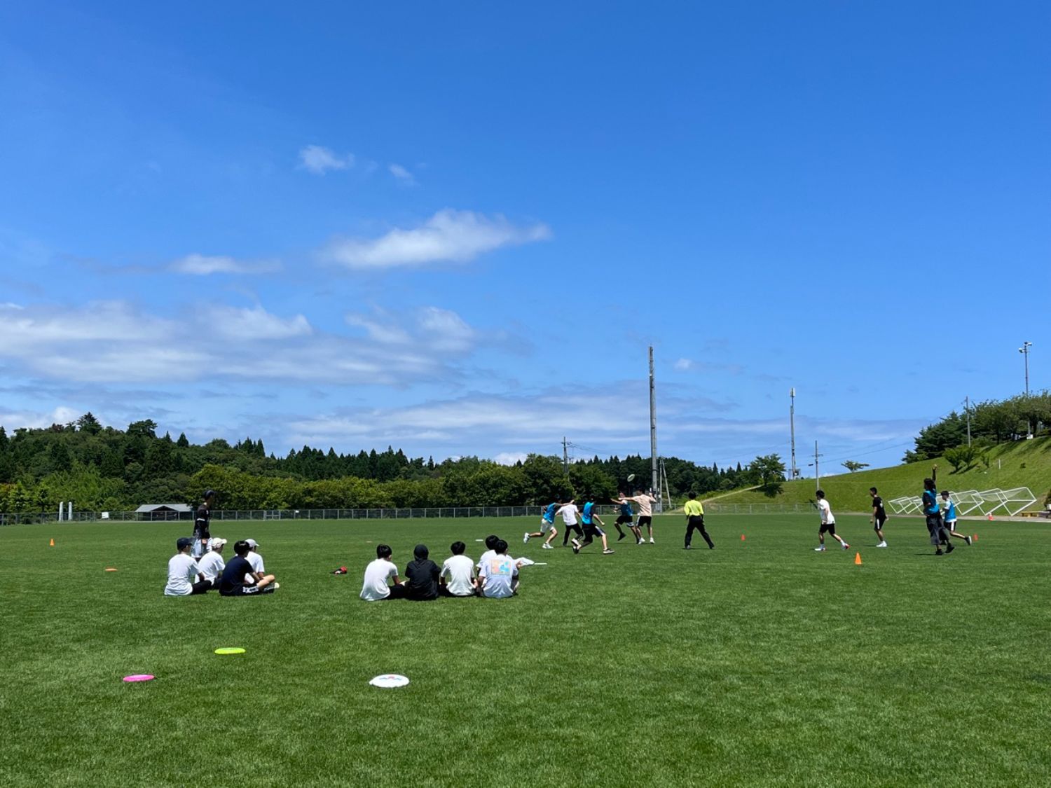 青空の下、広い芝生のフィールドで各チームに分かれて試合が行われている様子の写真