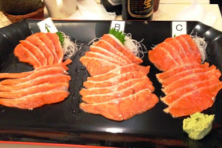 A・B・Cとラベルがつけられた三種類のサーモンの刺身が黒い皿に盛りつけられ、手前にわさびが添えられている写真