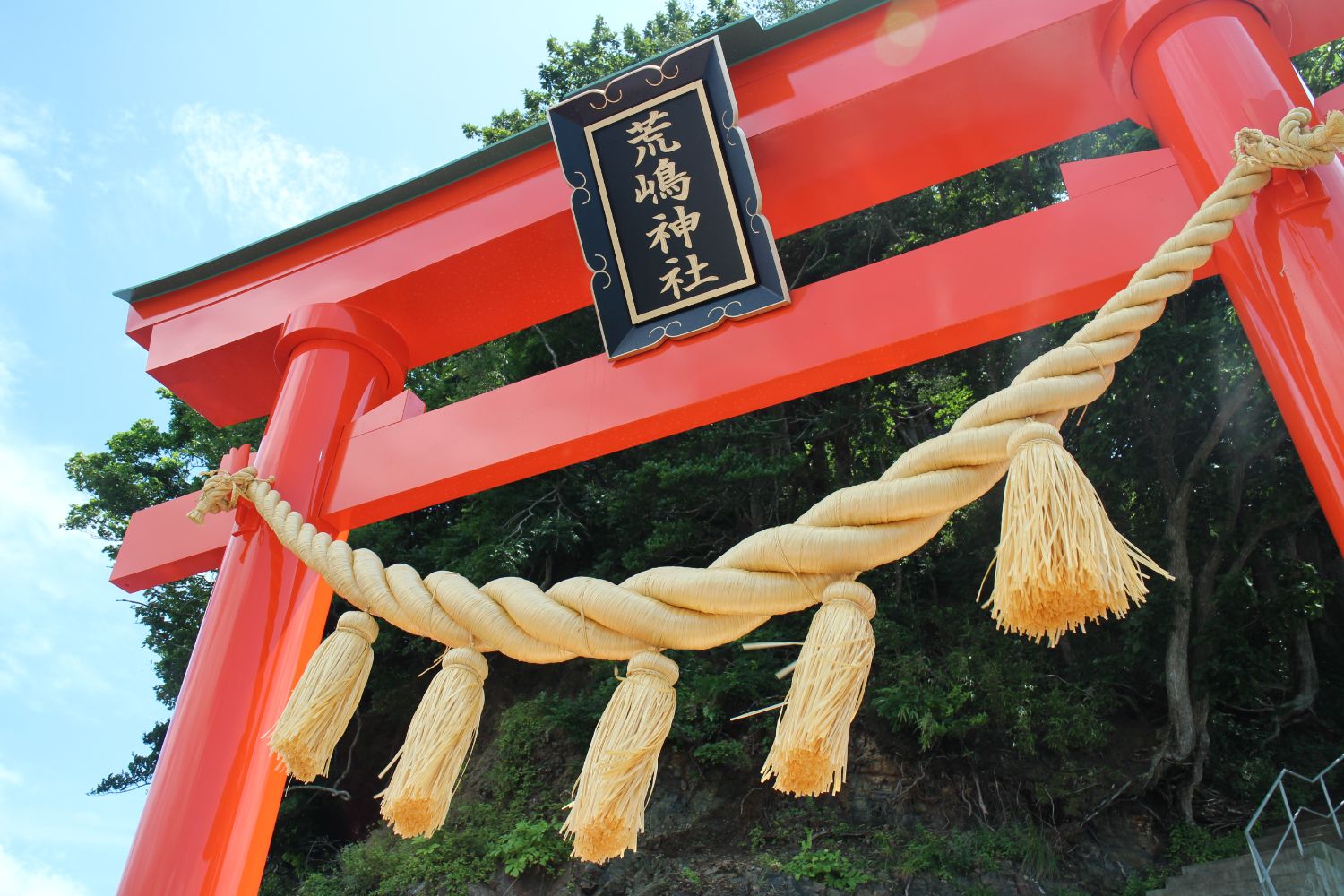 扁額に「荒嶋神社」と書かれ、立派なしめ縄が下がっている鮮やかな朱色をした鳥居を下から見上げるように写した写真