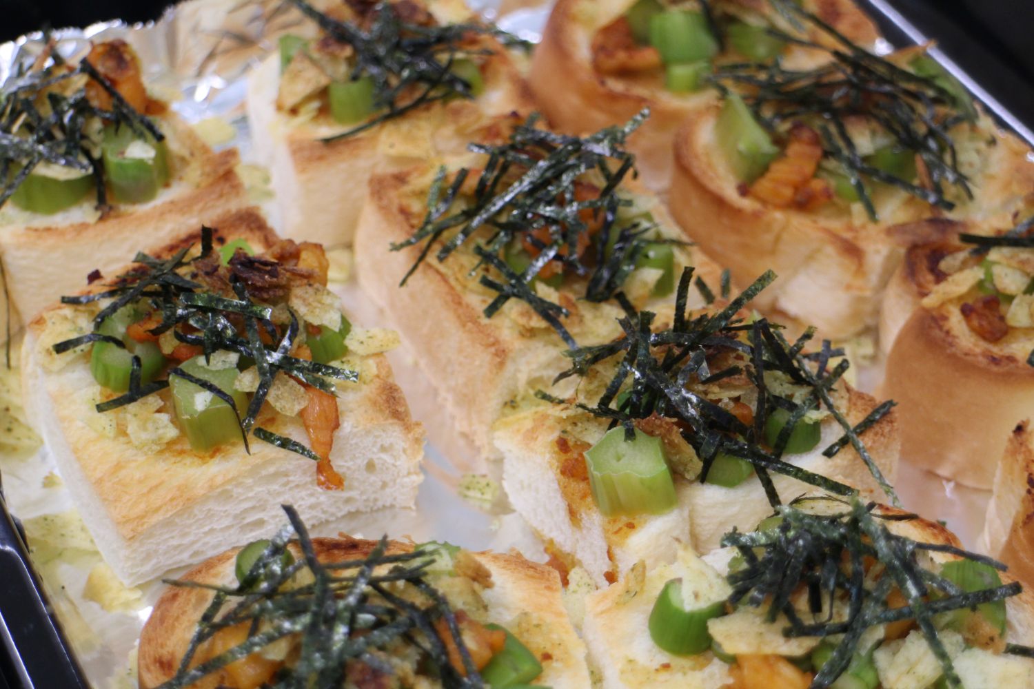 小さい四角に切った厚切りの食パンの上に、アスパラガスや細かく刻んで炒めたホヤ、砕いたポテトチップスを乗せてこんがり焼き、刻み海苔をトッピングした「ホヤのびっくりホヤパンマン」が並んでいる写真