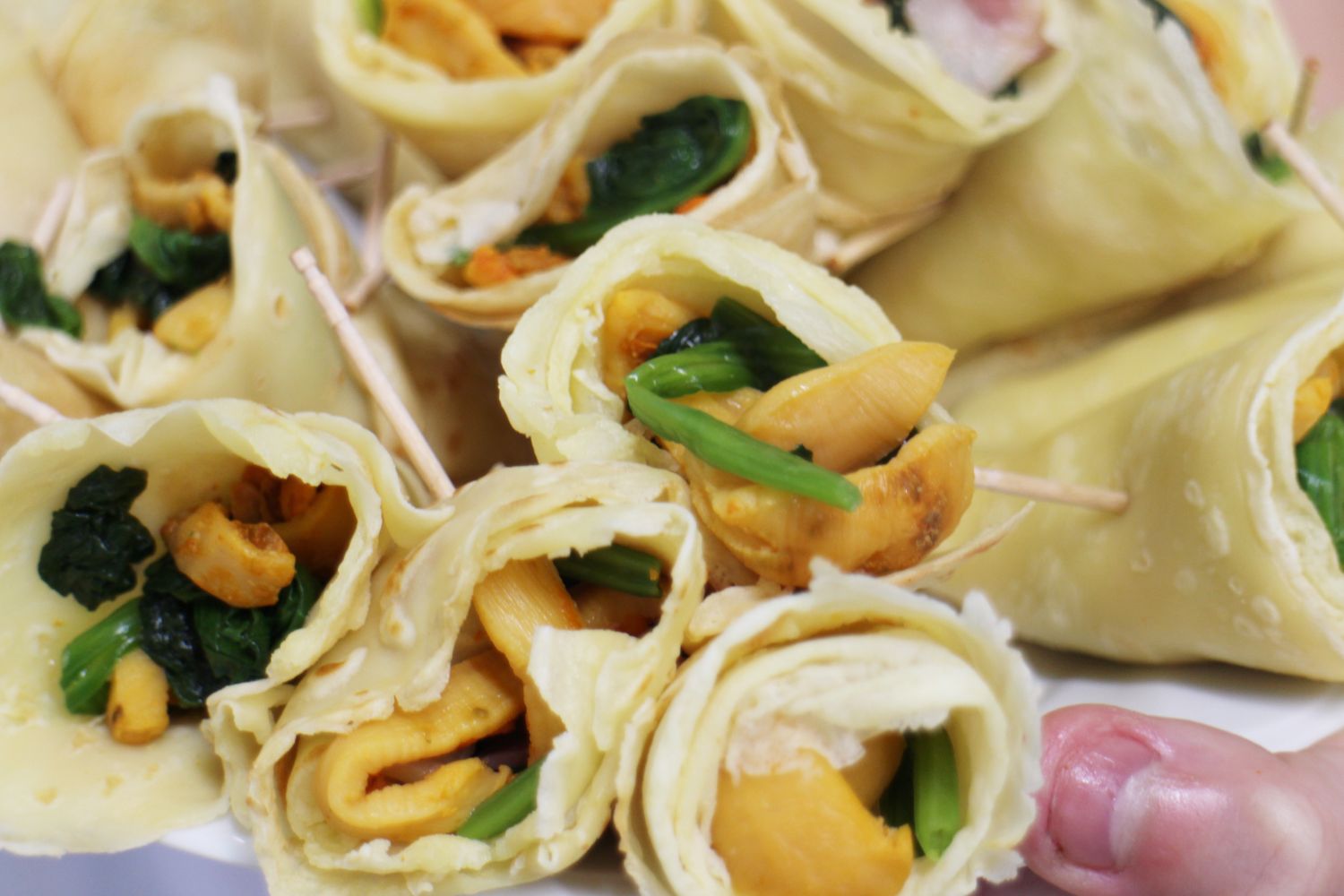 皿にたくさん並んでいる、ほうれん草とベーコン、細かく刻んだホヤをクレープ生地で包み、つまようじで留めたホヤットクレープをアップで撮影した写真