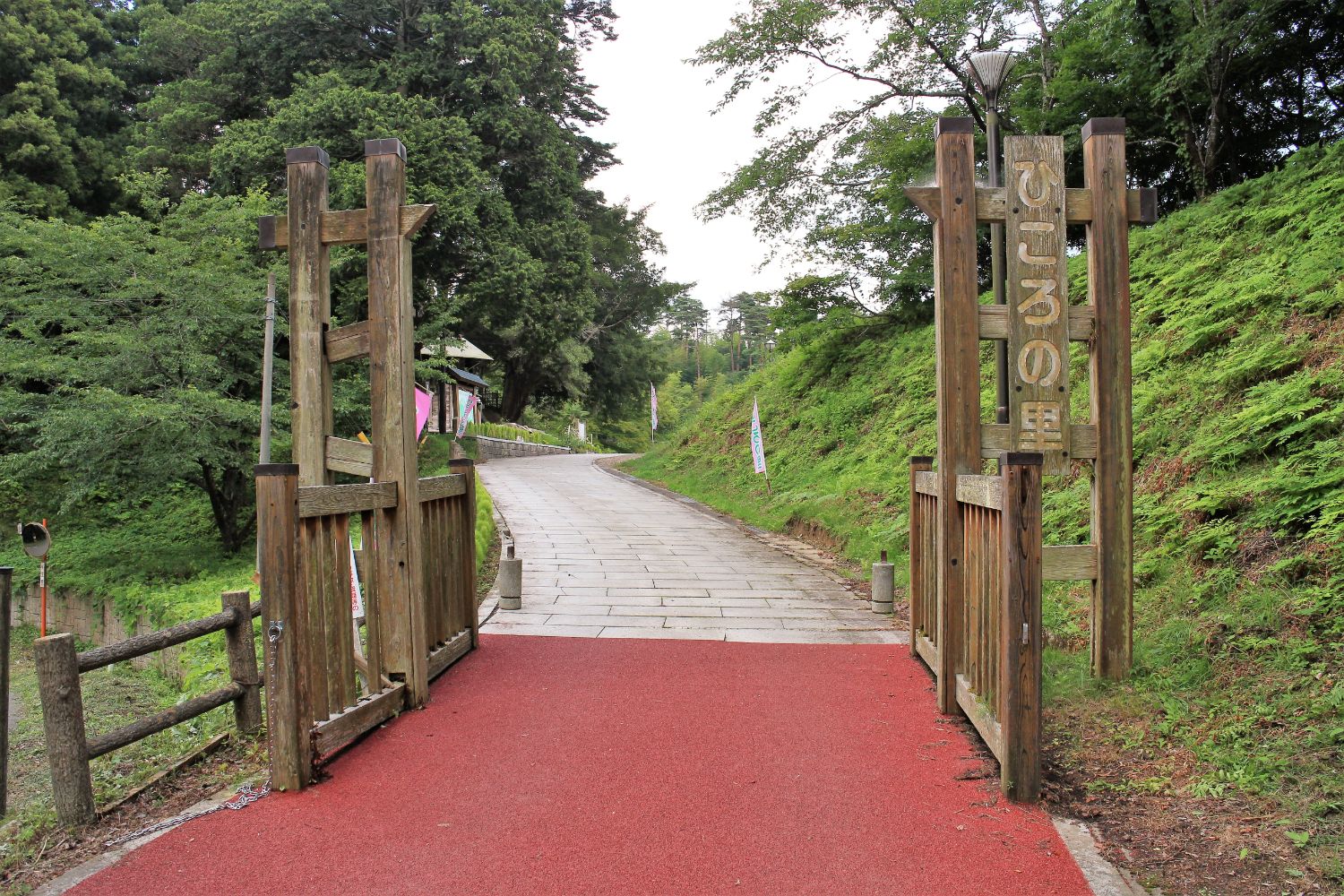 木々に囲まれた谷間にある、縦長の木の案内板『ひころの里』が設置された石畳の小径が続く風情ある入り口の写真