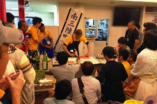 調理台を囲んで観客が座り、中央で漁師が魚のさばき方を実演しているイベントの写真