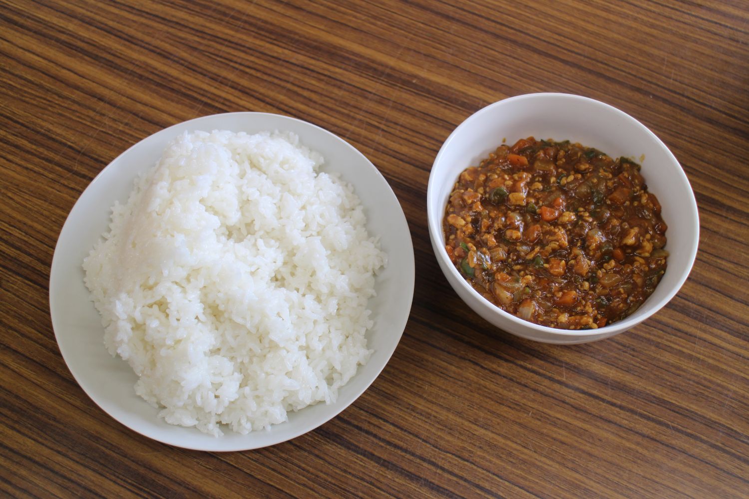 白い丸皿にご飯、白いお碗に細かく刻んだホヤとひき肉や野菜が入ったドライホヤカレーが盛り付けられ、木目調の机の上に並んでいる写真