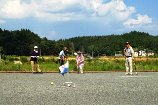 旗の立つゴール近くで男女数名の高齢者が真剣な表情でグラウンドゴルフをプレーしている様子を捉えた写真