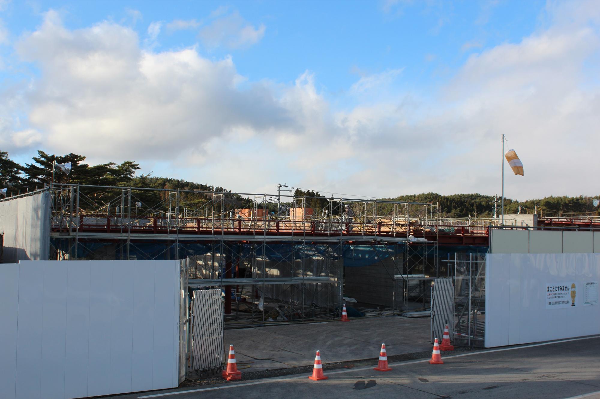 足場と型枠が高く組まれ、上部で作業する人の姿が見える、基礎から中間工程に進んだ建設現場の写真