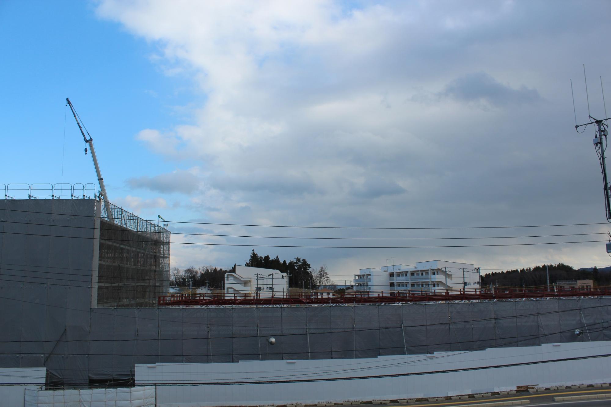 左側に防護シートに覆われた建設中の建物と大型クレーンが稼働している様子の平成28年12月6日現在の写真