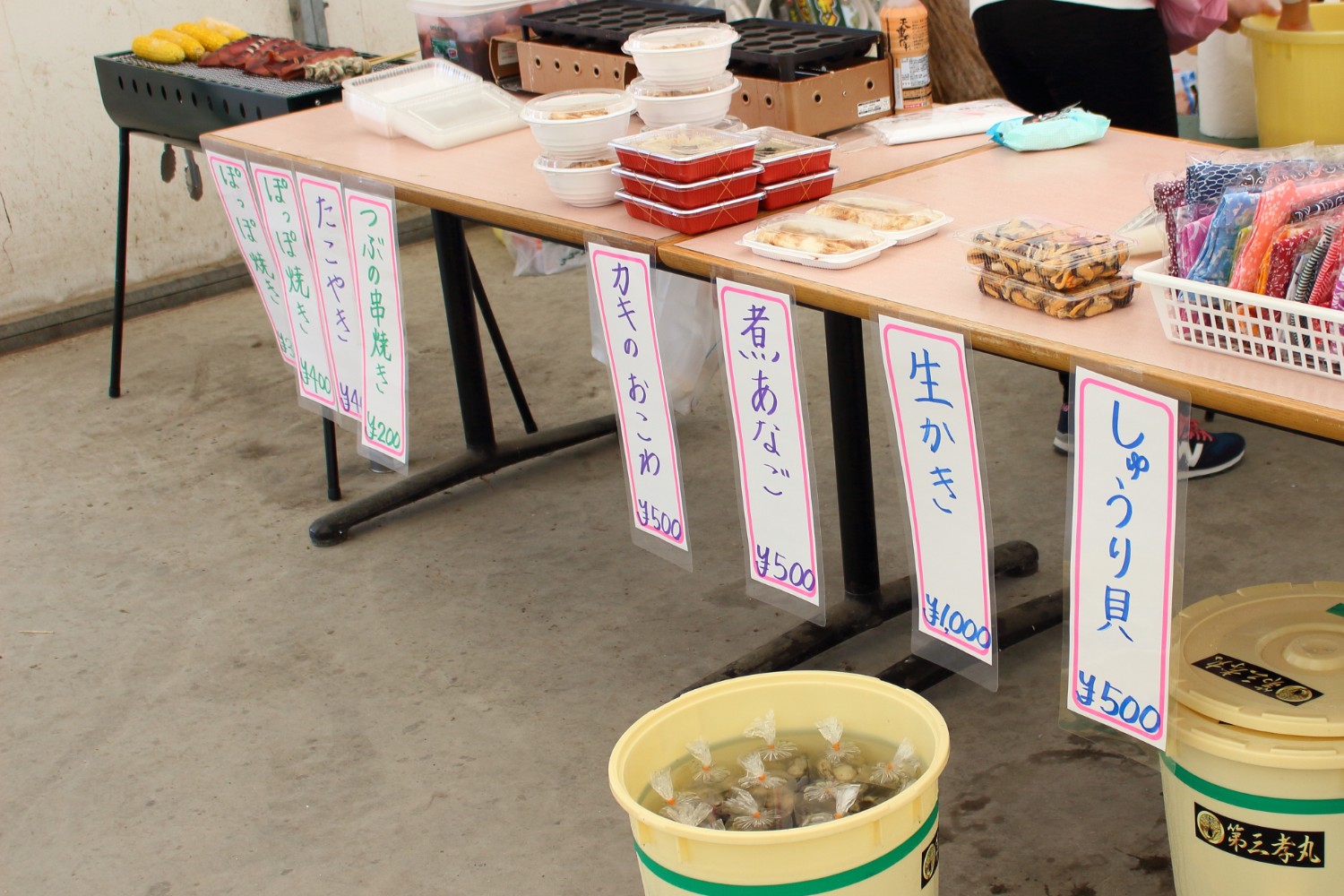 テーブルの上に、しゅうり貝・生かき・煮あなごなど様々な食品が並べられ、手前にはバケツに入った貝類が目立つように置かれている写真