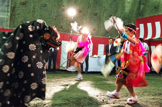 獅子舞と向かい合ったピンクの衣装を着た2人の子どもが扇を持って舞う姿が、トンネル内のステージで披露されている写真