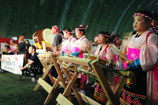 ピンクの衣装を着た子どもたちが、並んで太鼓を演奏しているところを側面から写した演奏中の写真