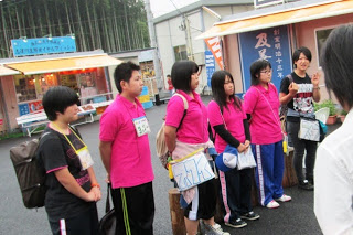 ピンク色のTシャツや黒のTシャツを着た南三陸町ボランティアサークルぶらんこのメンバー6名が並び、前方の人の話を聞いている様子の写真