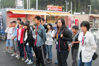 商店街の前で参加者のこどもたちが並び、真剣な表情で説明を聞いている様子の写真