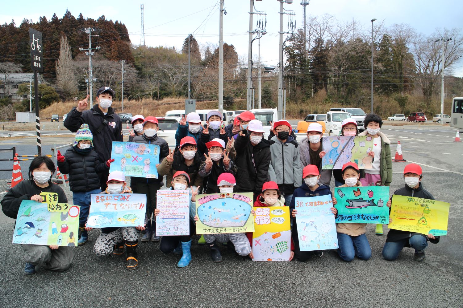 子どもたち約20人が屋外の駐車場でマスクを着け、赤や白の帽子をかぶりながら、それぞれがカラフルな手書きのポスターを手に持ち、「ゴミを拾おう」「海にゴミを捨てないで」など環境保護を呼びかけている集合写真