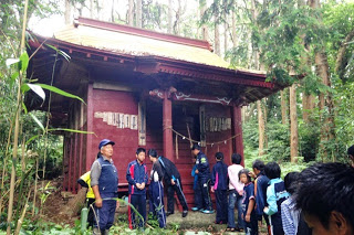 深い森の中に佇む赤い社殿に、引率された子どもたちが一列に並びながら説明を聞いている写真