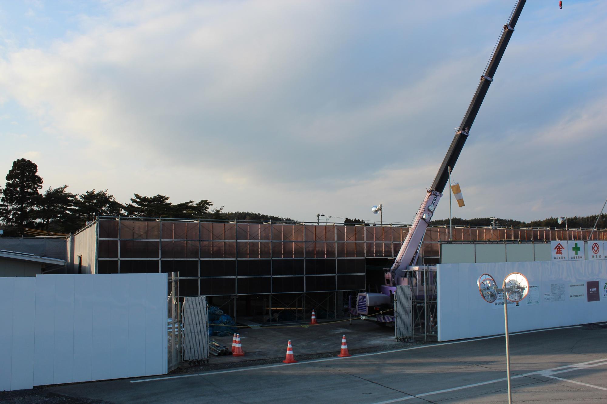 鉄骨の組み立てが進みクレーンが作業中で、建物の形が少し見えてきた中間段階の建設現場の写真