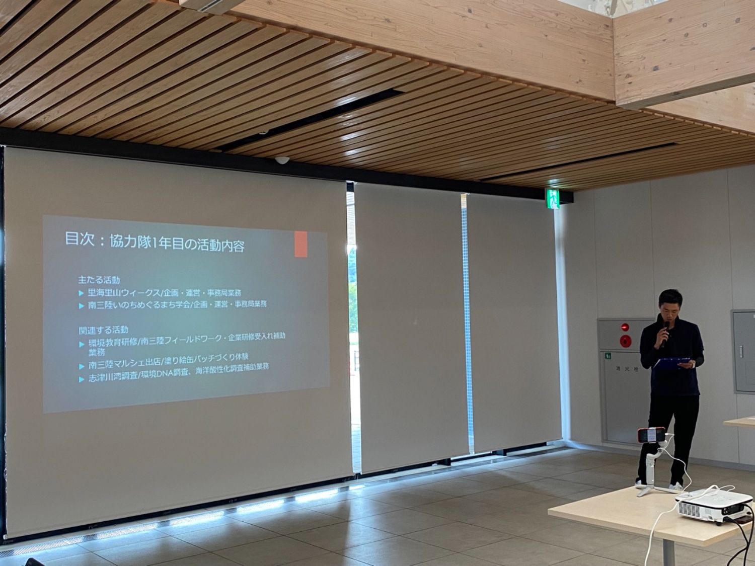 小林さんがマイクと資料を持ってスライドを見ながら発表をしている写真